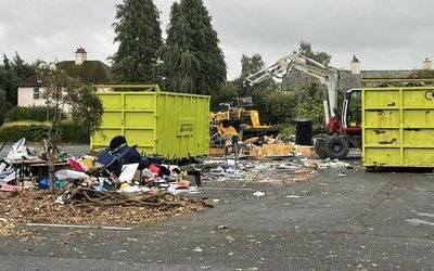Two skips beside a large pile of mixed waste on a site