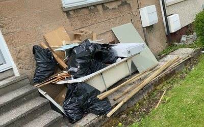 Bags, timber and an old bath outside the front steps of a house