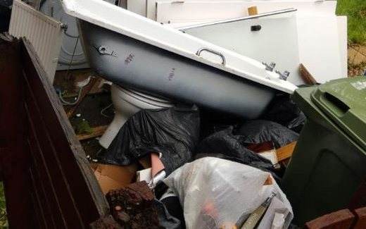 Old bath, toilet, radiator and timber piled up in a front garden