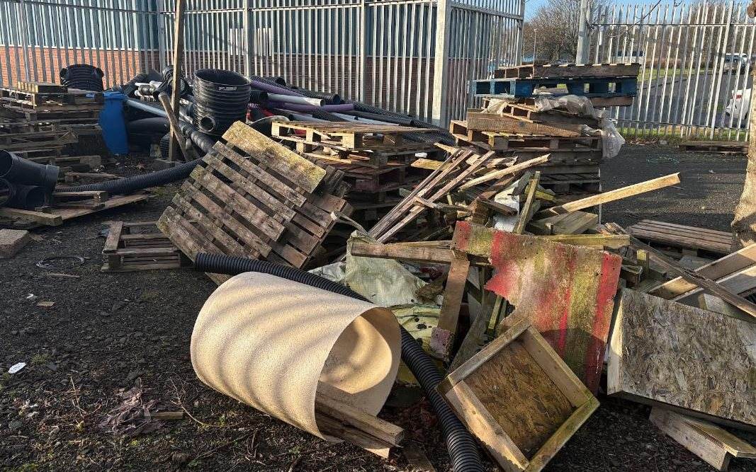 Pallets, pipes and timber dumped in a fenced yard